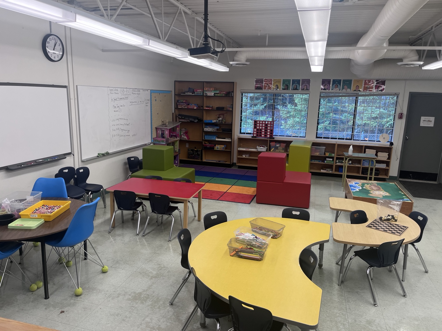 A bright classroom with round tables, books, games, open floor space, and colourful soft seating