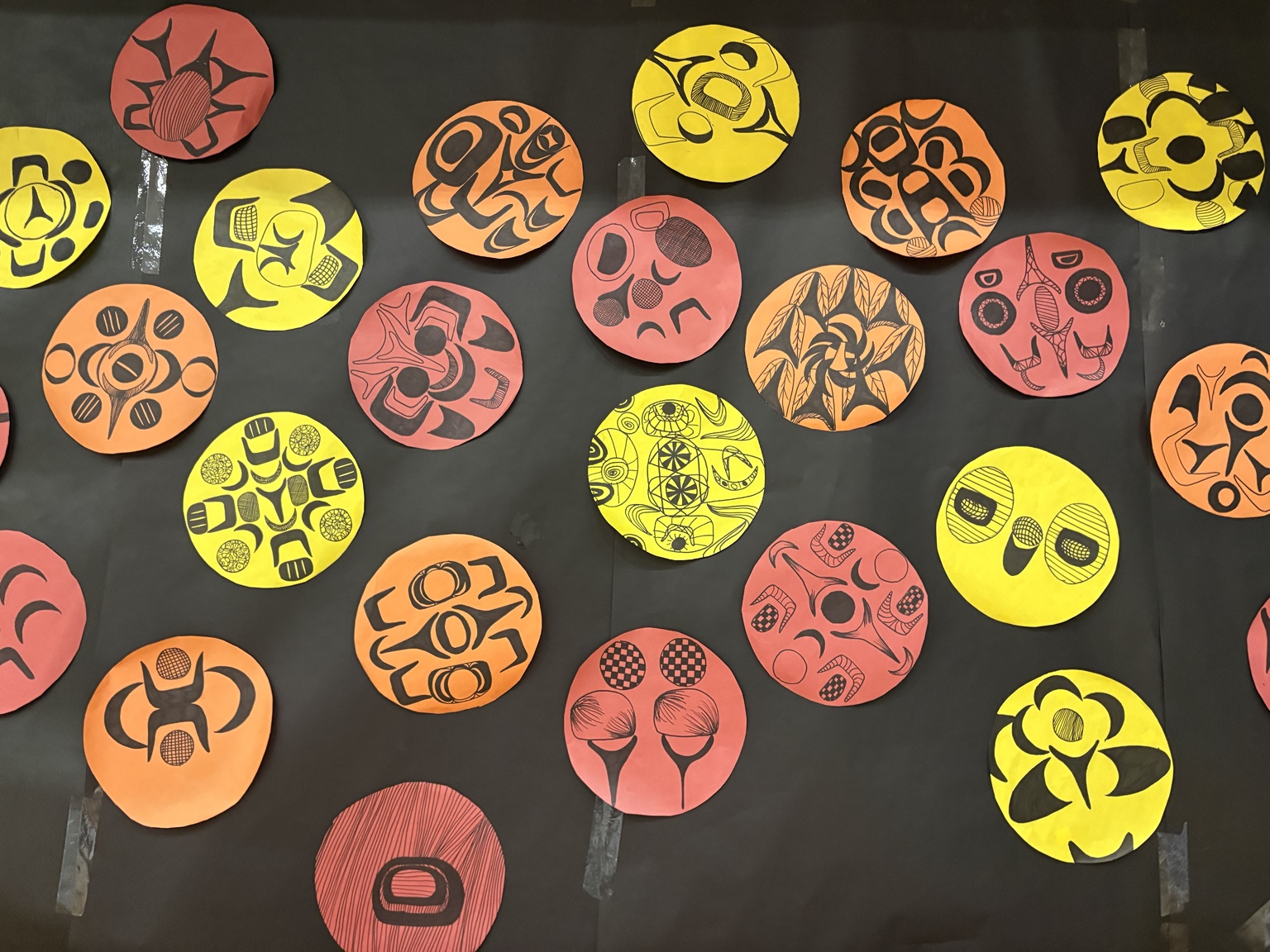 A classroom display of colourful circular student prints inspired by Northwest Coast forms